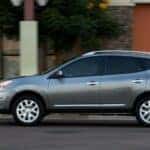 A gray 2013 Nissan Rogue for sale near Urbana is shown driving on a city street.