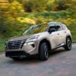 A tan 2024 Nissan Rogue is shown rounding a corner.