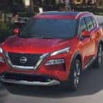 A red 2024 Nissan Rogue for sale near Urbana is shown driving on a city street.