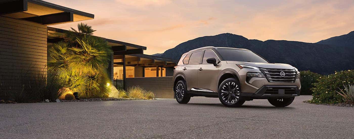 A silver 2024 Nissan Rogue Platinum parked outside a home at dusk.