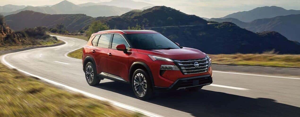 A red 2024 Nissan Rogue is driving on a winding open road.