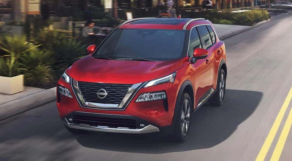 A red 2024 Nissan Rogue Platinum is shown driving on a city street.