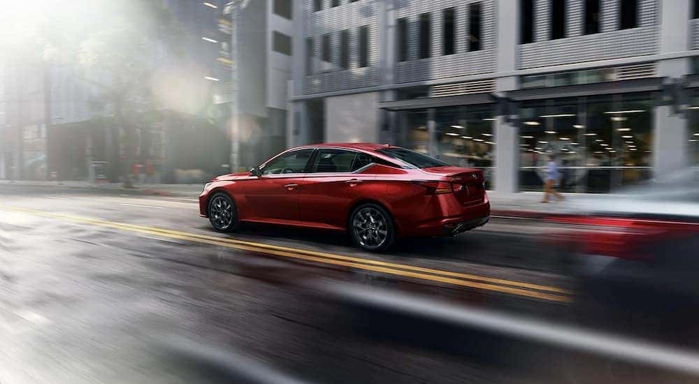 A red 2023 Nissan Altima is shown driving on a city street.