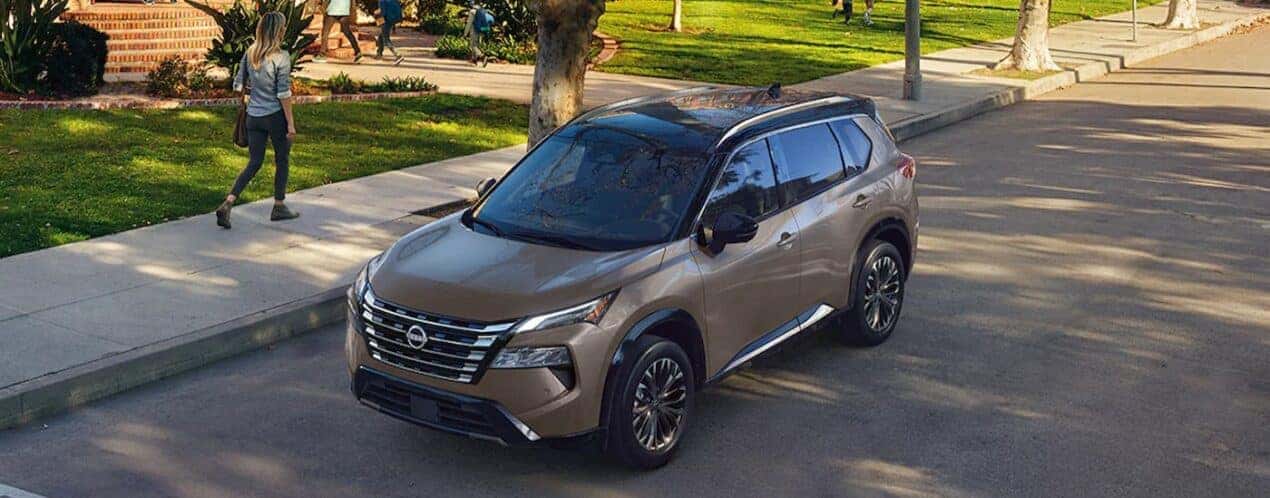 A tan 2024 Nissan Rogue is shown parked near a person walking.
