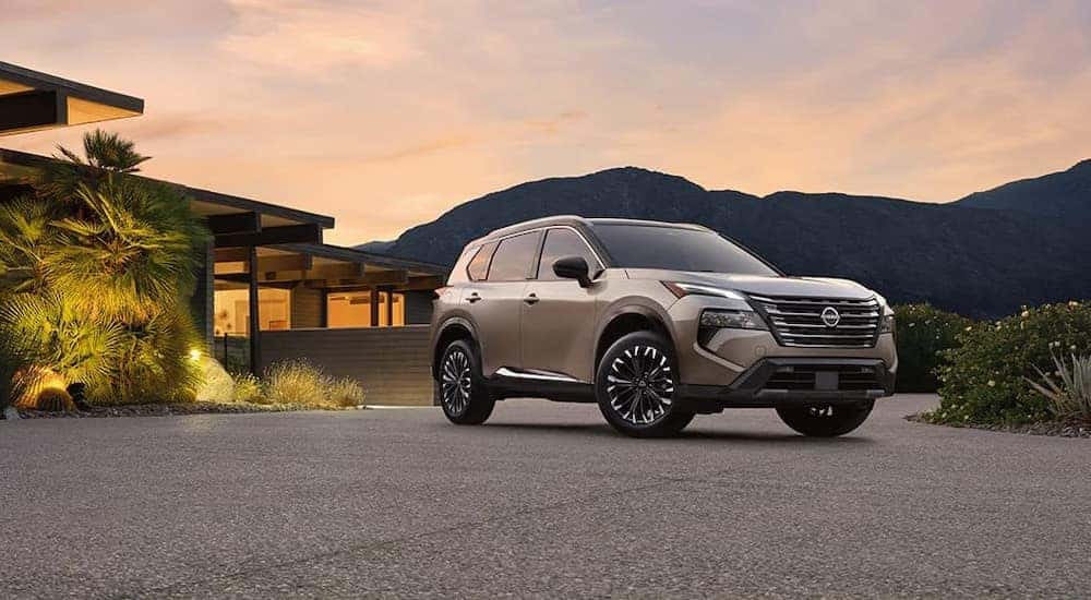 A tan 2024 Nissan Rogue Platinum is shown parked near a house.