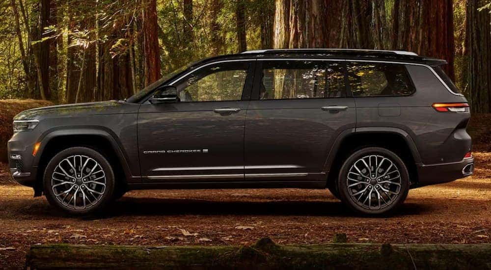 Side view of a grey 2023 Jeep Grand Cherokee L parked in the woods.