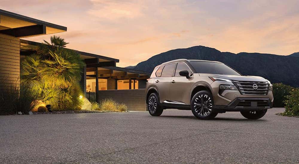 A silver 2025 Nissan Rogue Platinum parked in front of a house at dusk.
