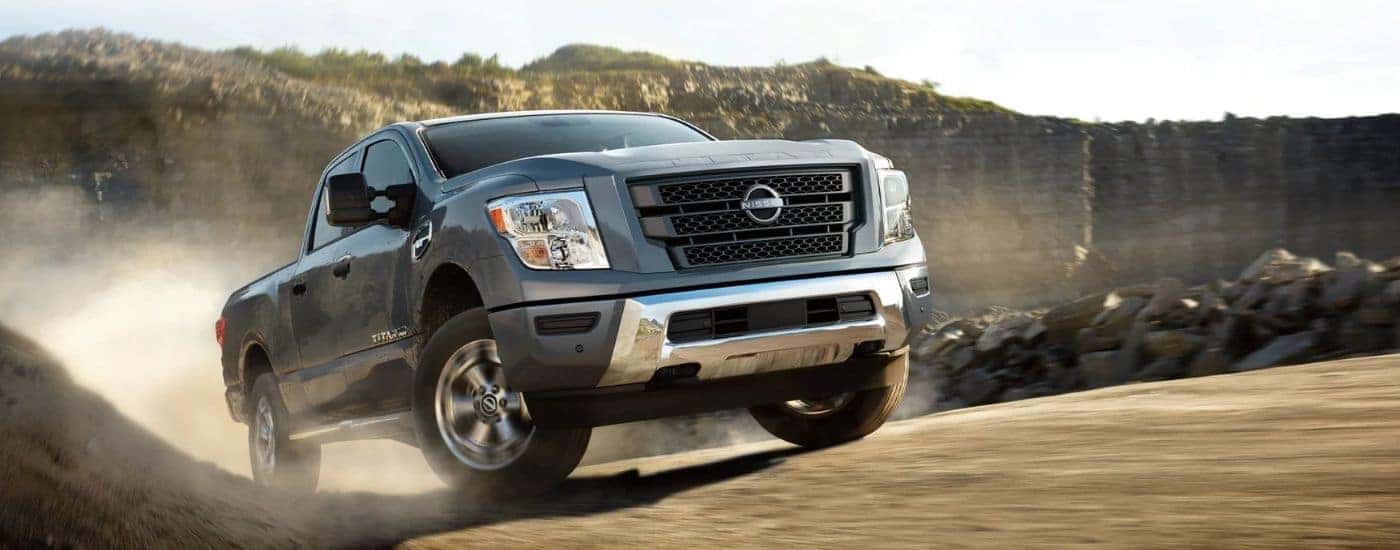 A silver 2024 Nissan Titan XD driving on a dusty dirt road.