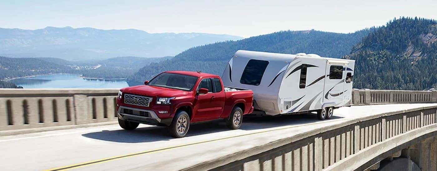 A red 2024 Nissan Frontier is shown towing a trailer on a bridge.