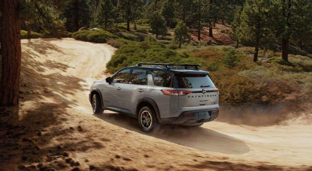 Rear angled view of a grey 2025 Nissan Pathfinder Rock Creek driving down a dirt road.