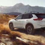 Rear view of a white 2025 Nissan Rogue Platinum AWD driving through an arid landscape.