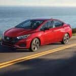 Left-angled view of a red 2025 Nissan Versa driving down a road.