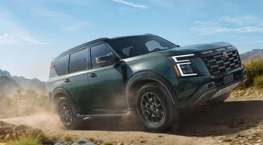 A green 2025 Nissan Armada Pro-4X driving off-road from a dealer with a Nissan Armada for sale.