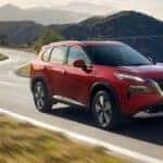 A red 2025 Nissan Rogue driving on a highway.