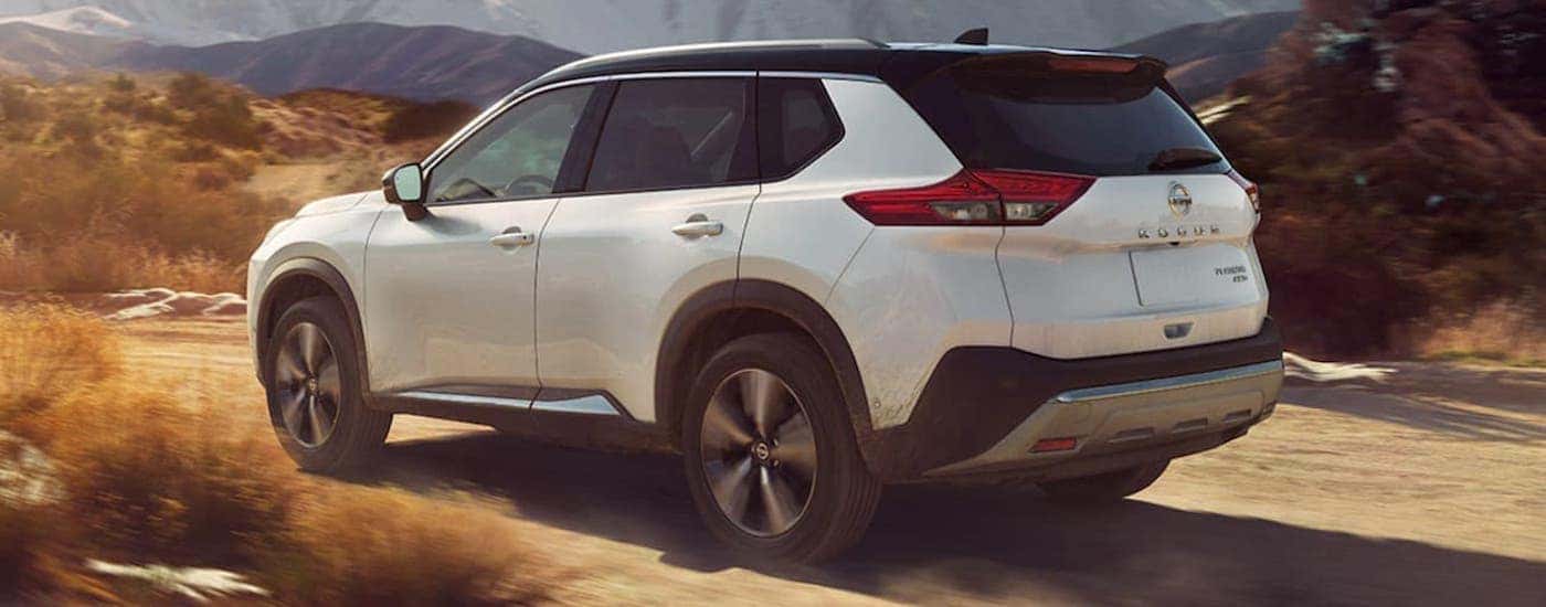 Rear view of a white 2021 Nissan Rogue driving on a trail.