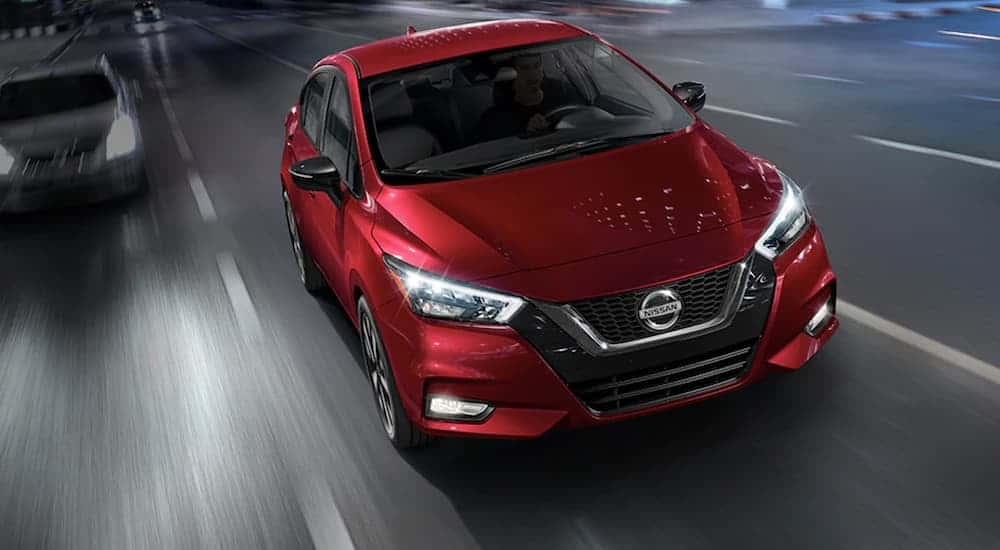 A red 2021 Nissan Versa driving to a used Nissan dealer.