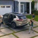A tan 2026 Nissan Rogue parked near a home.