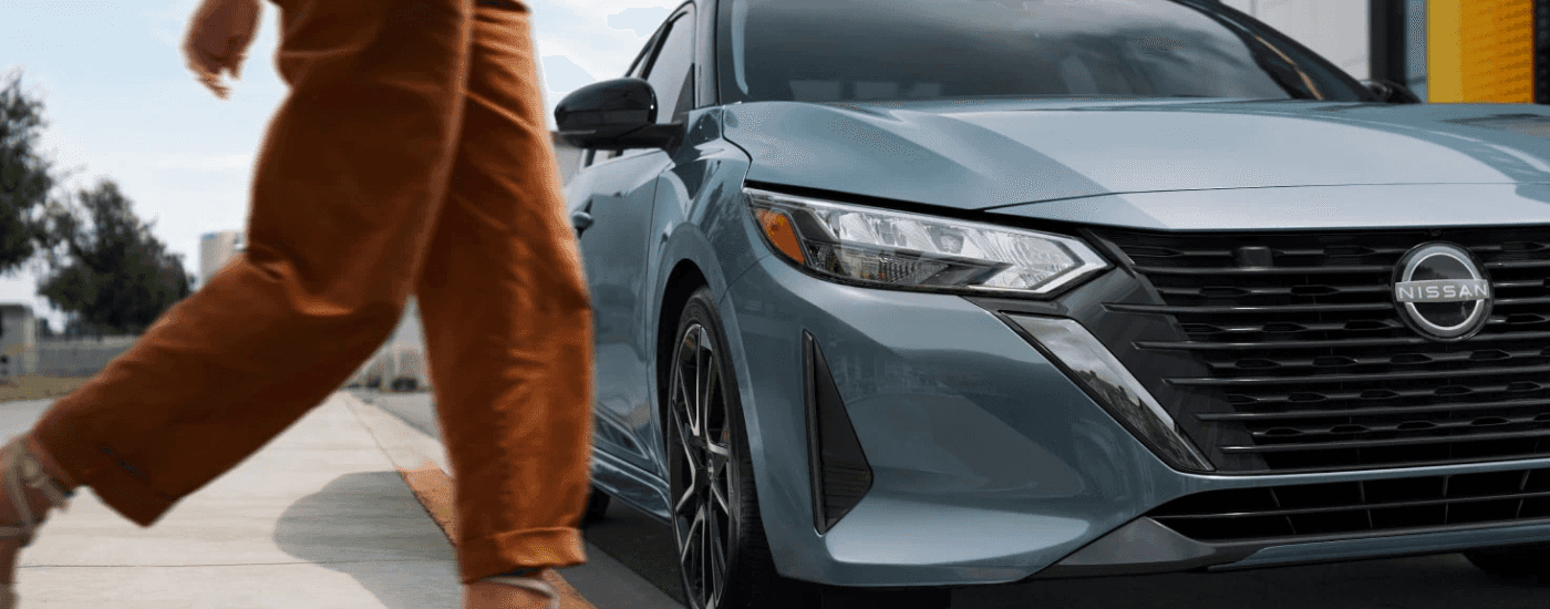 A person walks past the front end of a blue 2025 Nissan Sentra