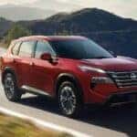 A red 2026 Nissan Rogue driving on a highway.