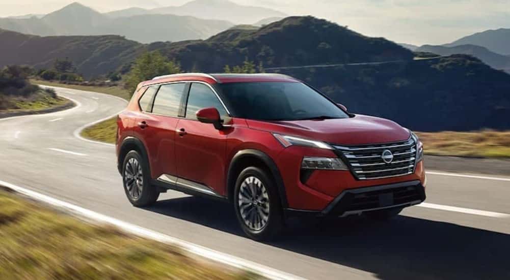 A red 2026 Nissan Rogue driving on a highway.