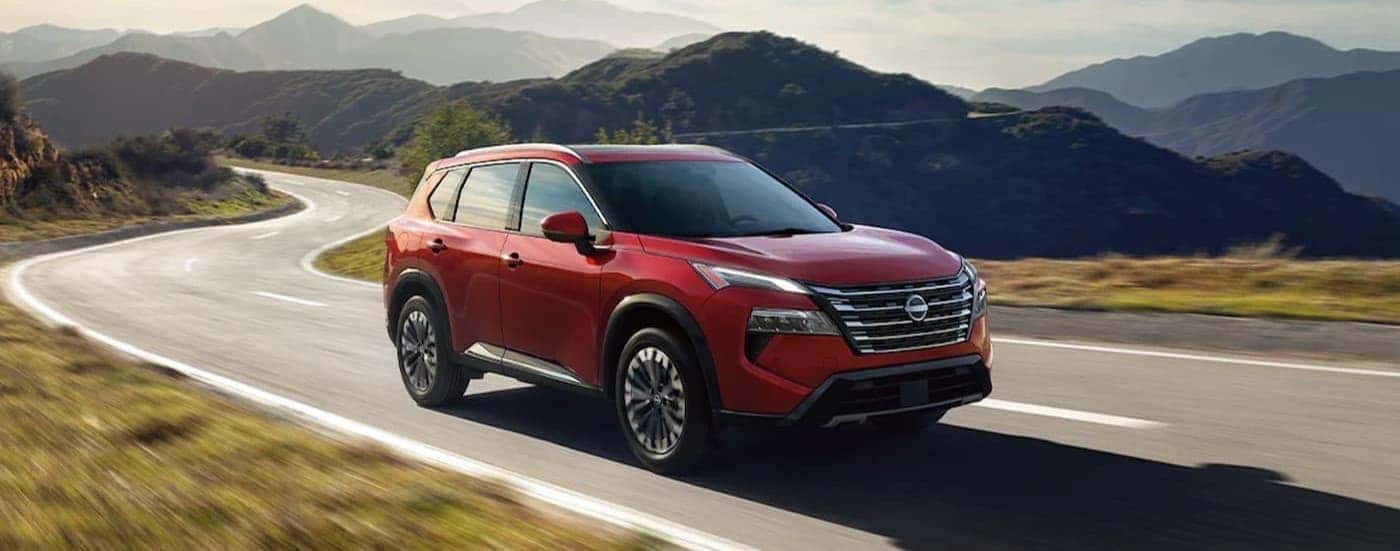 A red 2026 Nissan Rogue driving on a highway.