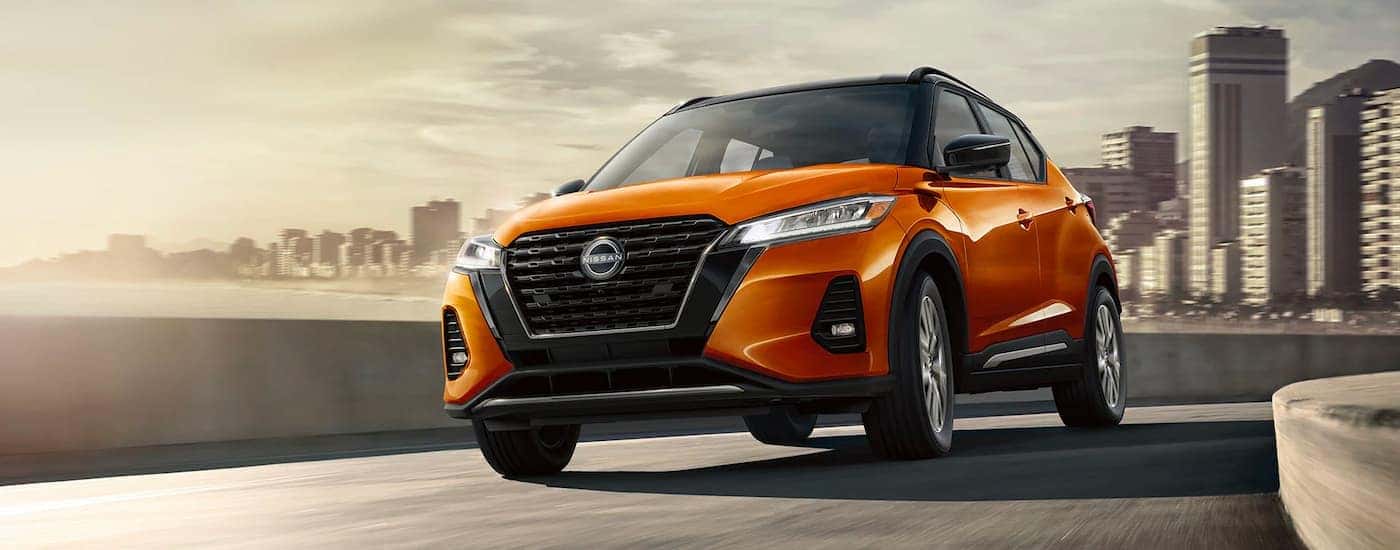 Orange 2023 Nissan Kicks driving away from city.