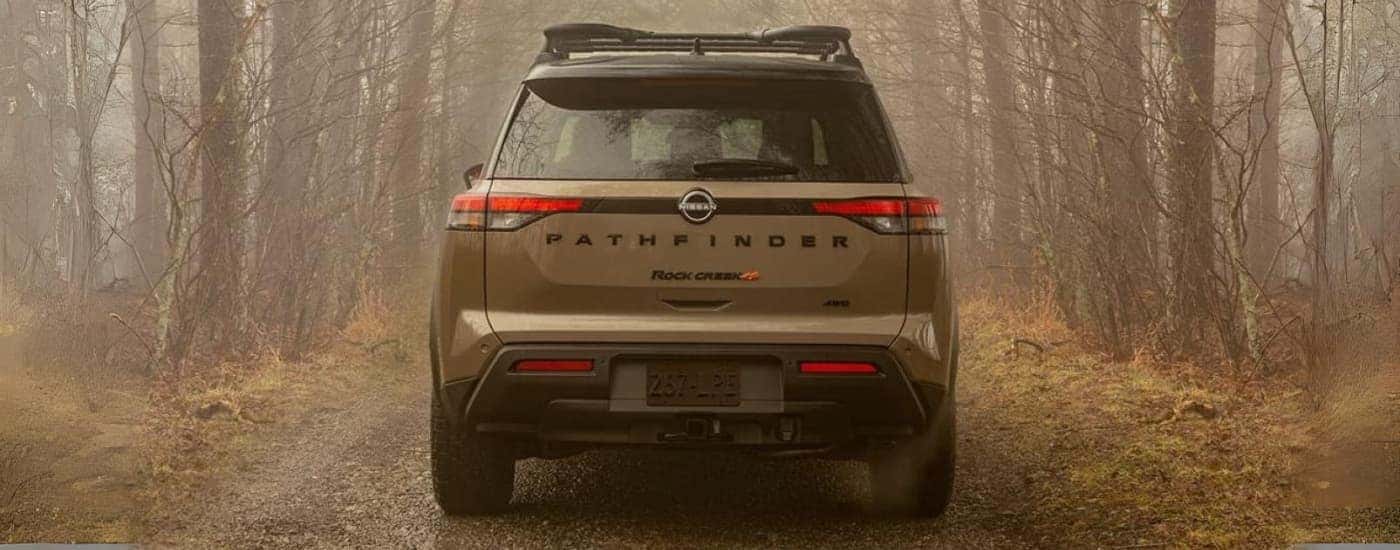 Brown 2023 Nissan Pathfinder shown from the rear driving through the woods