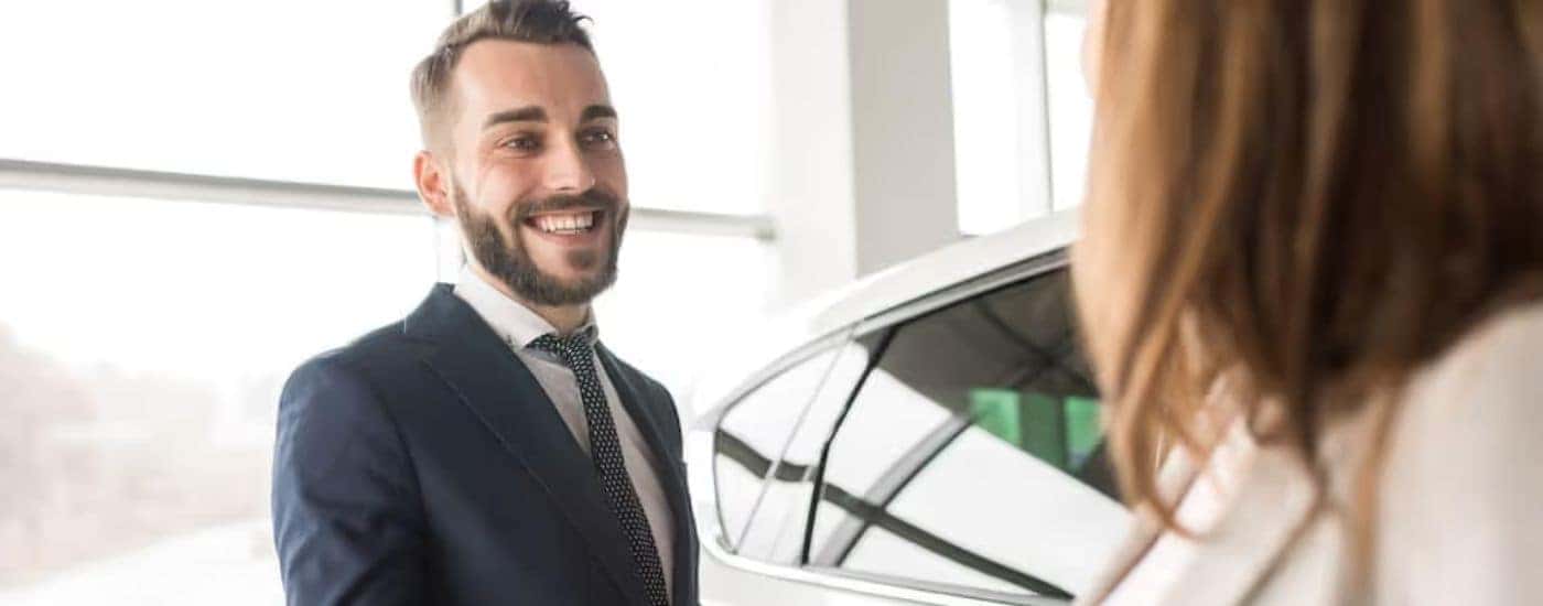 A salesman is passing a set of keys to a woman at a Nissan Rogue dealer.