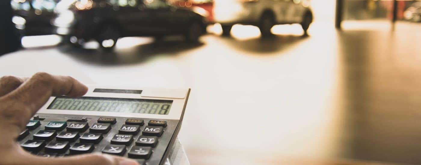 A person is shown using a calculator at a car dealership