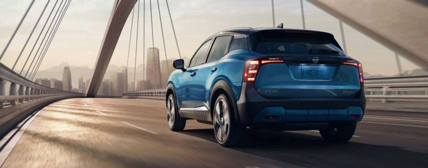 Blue 2026 Nissan Kicks rear view driving over a bridge.