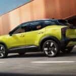 A yellow 2026 Nissan Kicks SR AWD shown driving on a paved road by a bridge.