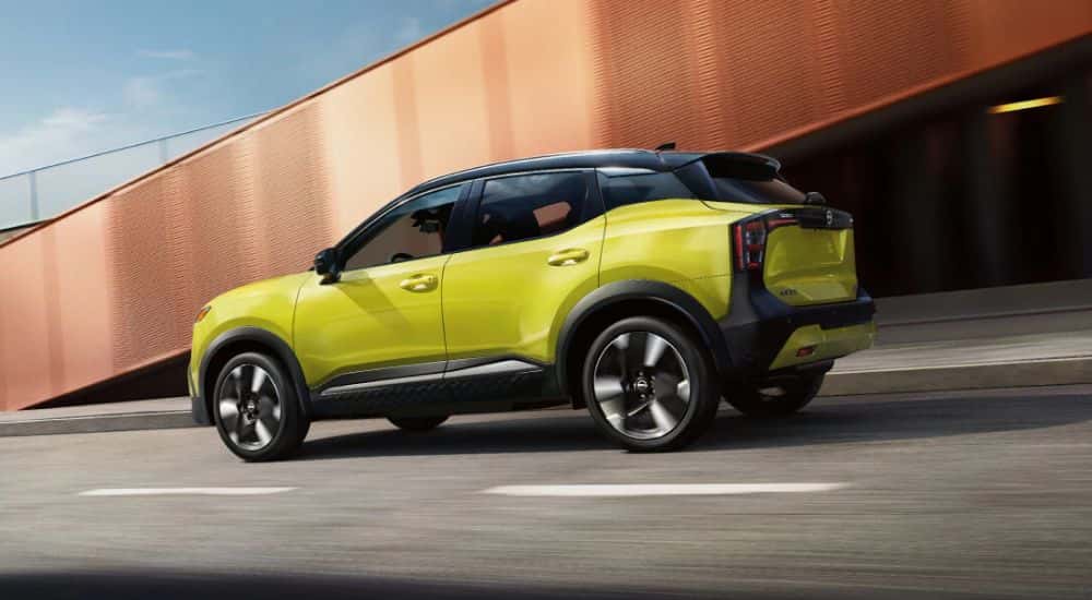 A yellow 2026 Nissan Kicks SR AWD shown driving on a paved road by a bridge.