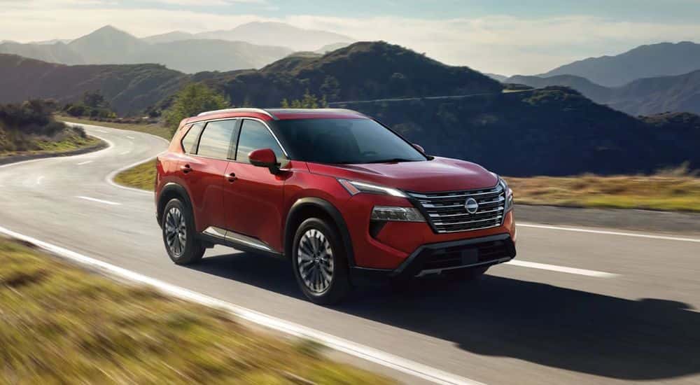 A red 2026.5 Nissan Rogue Platinum AWD driving a mountain-lined road.