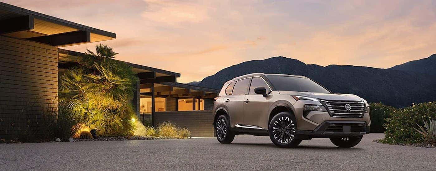 A tan 2024 Nissan Rogue parked near a house.