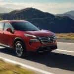 Red 2026 Nissan Rogue Platinum driving on a paved road.