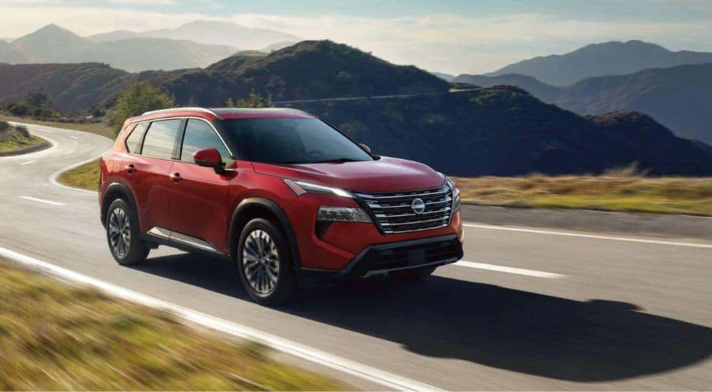 Red 2026 Nissan Rogue Platinum driving on a paved road.