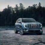 A blue 2024 GMC Acadia Denali is shown parked near a lake and cabin after leaving a GMC dealer.