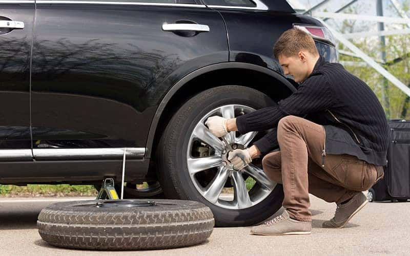 Man changing a flat tire on the side of the road