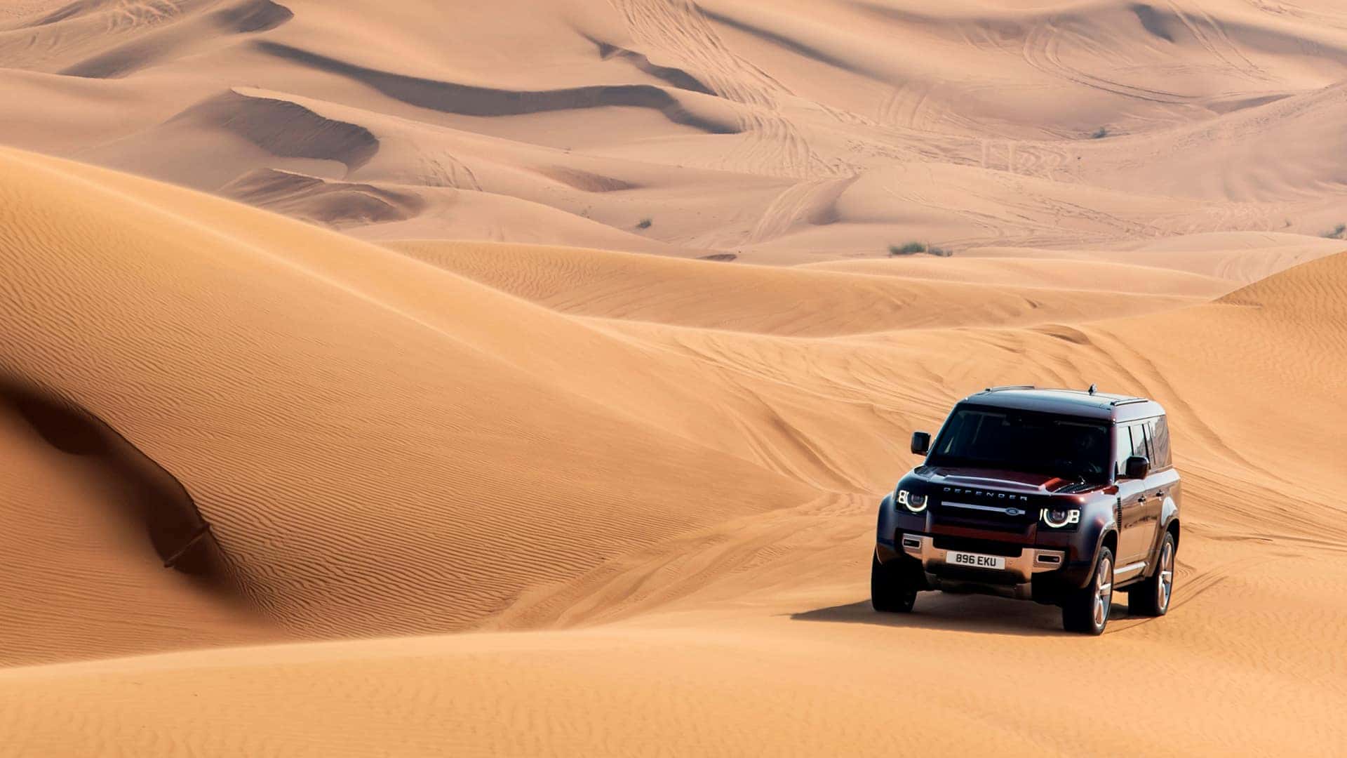 A red 2025 Range Rover Defender driving through a desert.