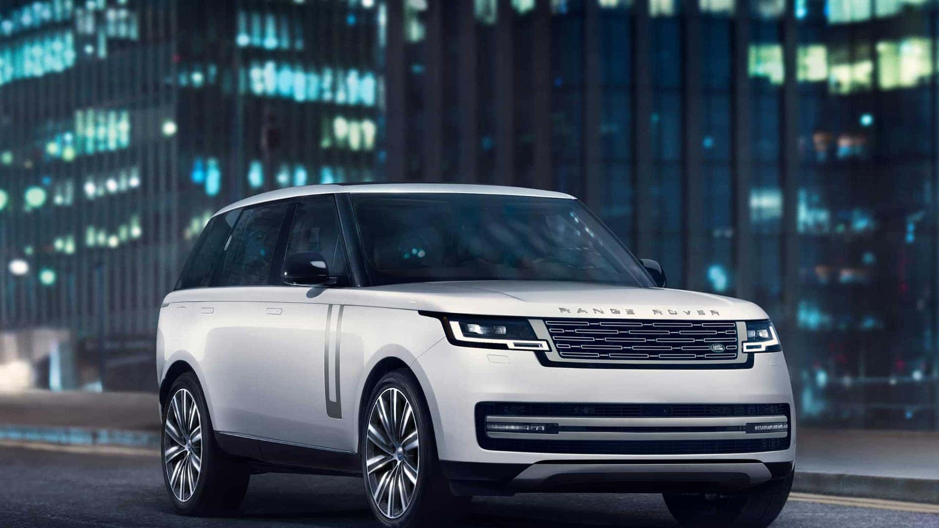 A white 2025 Range Rover driving through a city at night.