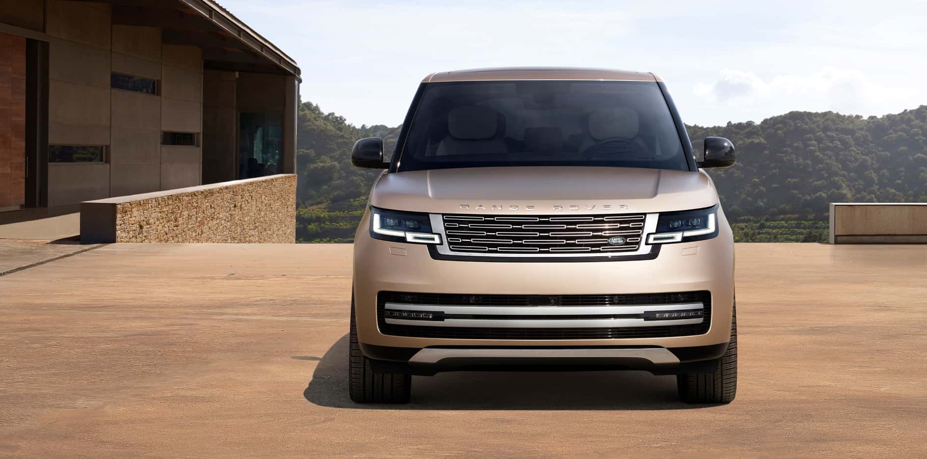 A front view of a light brown 2026 Range Rover parked by a nice house.