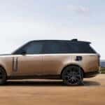 A tan Range Rover electric model in profile, plugged into a wall and charging.