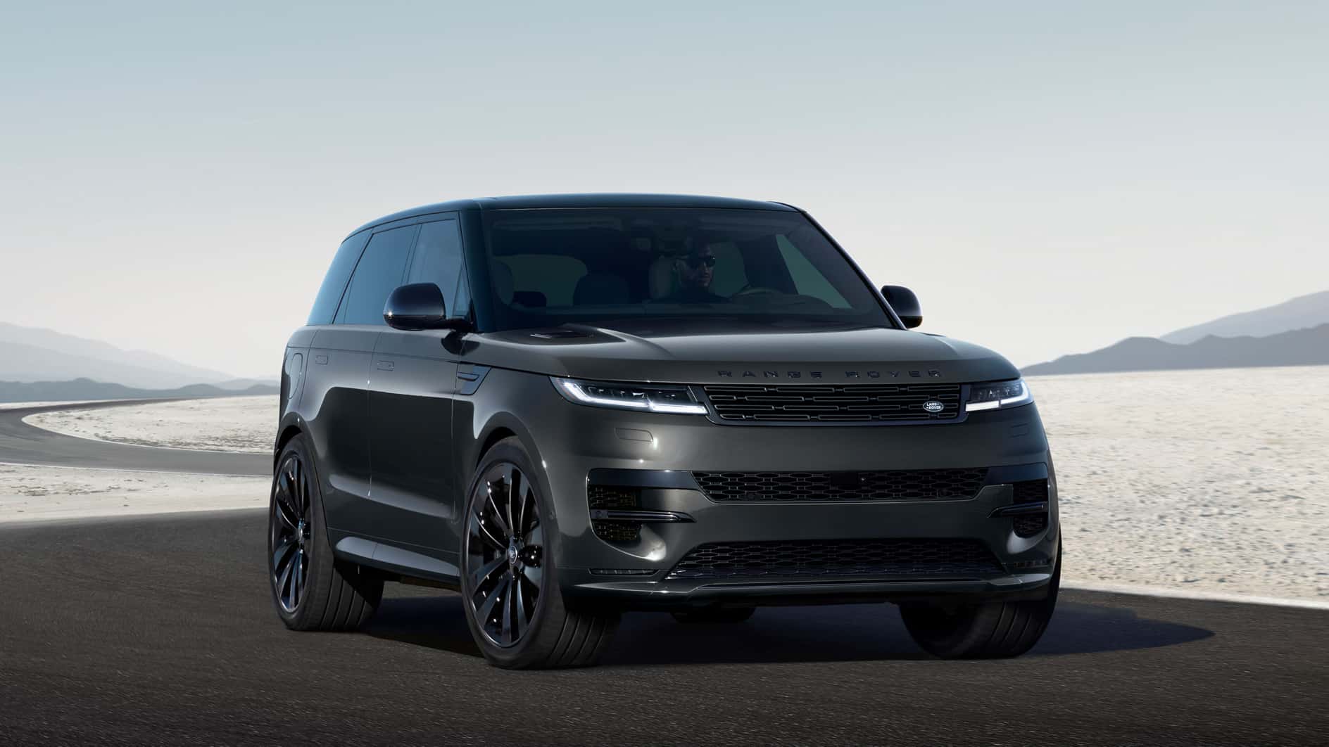 A black Range Rover Sport driving down a winding road in a flat desert.