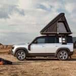 A silver Defender 110 being used for camping in a desert.