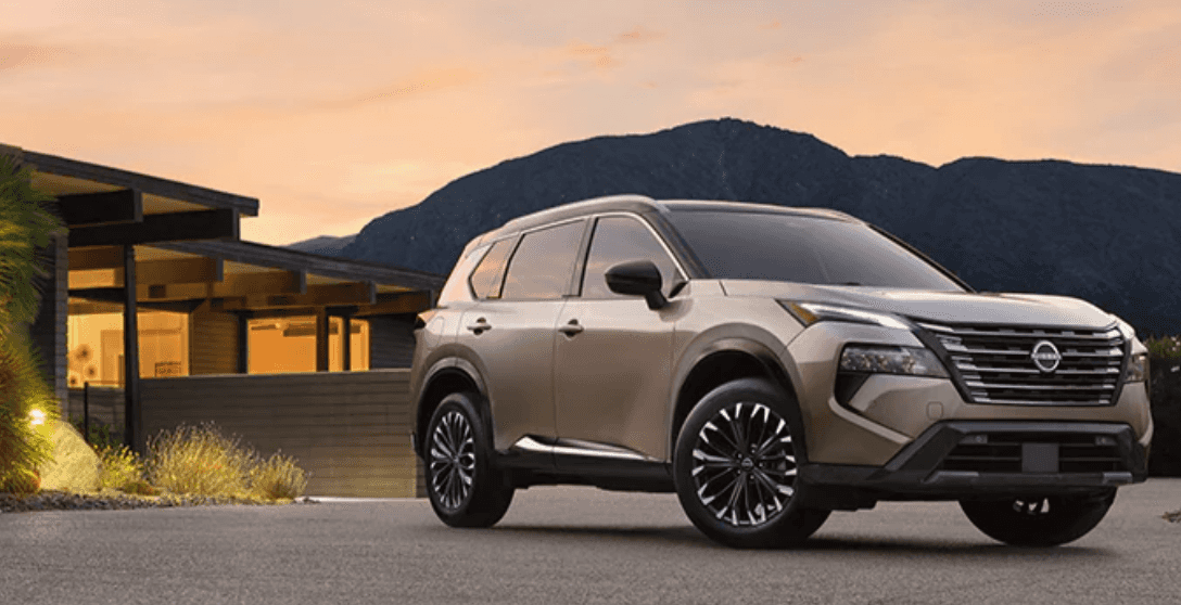 A beige 2024 Nissan Rogue Platinum AWD in front of a home and desert landscape at sunset