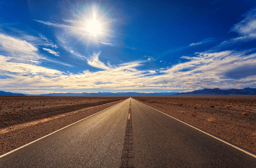A two-lane asphalt highway stretching into the desert under a bright blue sky