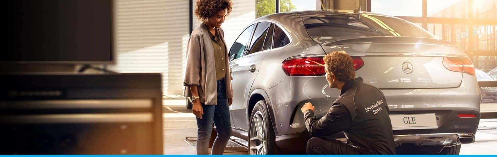 Woman watches as car dealership technician points to car