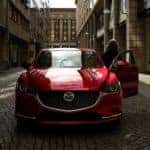 A red 2018 Mazda6 is shown from the front parked on a city street.