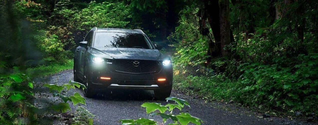 A grey 2023 Mazda CX-50 is shown driving down a trail in the woods.