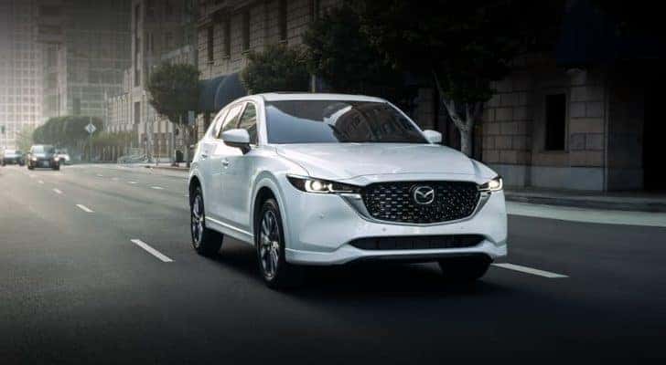 A white 2022 Mazda CX-5 is shown driving on a city street after leaving a Mazda CX-5 dealer near you.